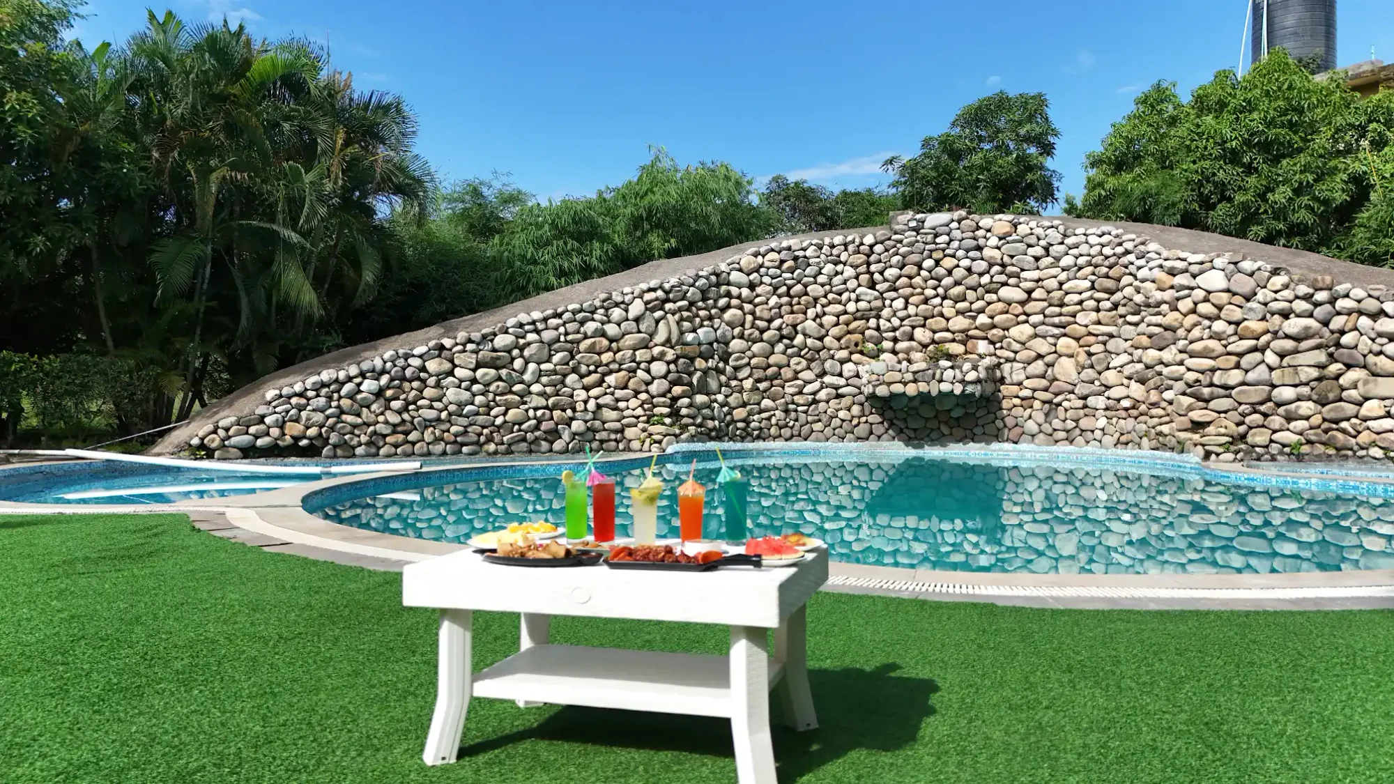 A table beside the pool and stone waterfall wall